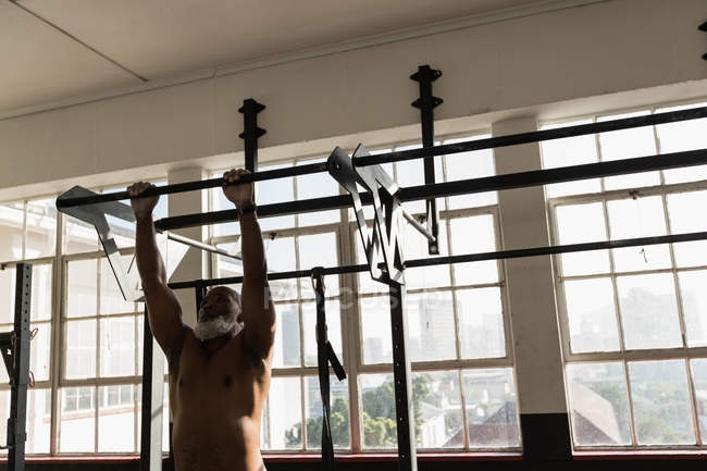 Homem sênior determinado exercitando puxar para cima na barra de puxar no estúdio de fitness . — Fotografia de Stock