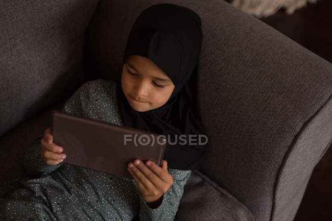 Primer plano de la chica musulmana acostada en el sofá y el uso de la tableta digital - foto de stock