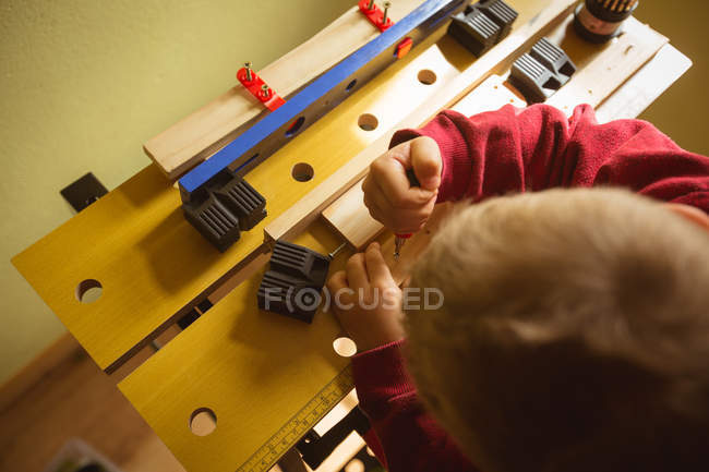 Menino usando ferramenta na prancha de madeira em casa — Fotografia de Stock