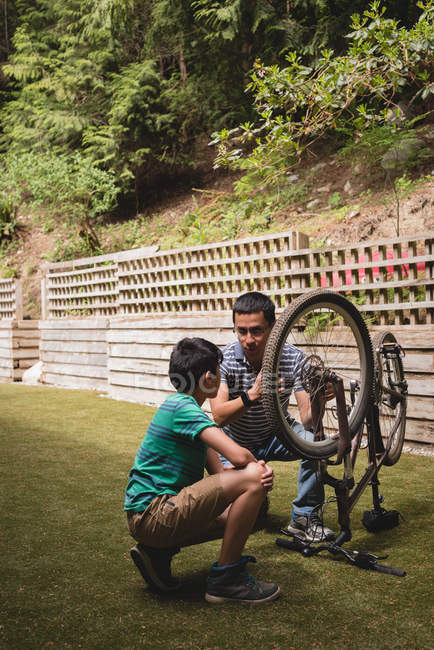 Père et fils interagissent les uns avec les autres pendant la réparation du cycle dans le jardin — Photo de stock