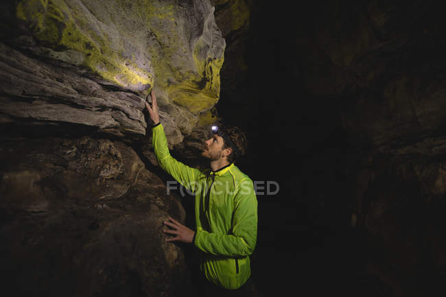 Пішохід оглядає скелі в темній печері з факелом голови — стокове фото
