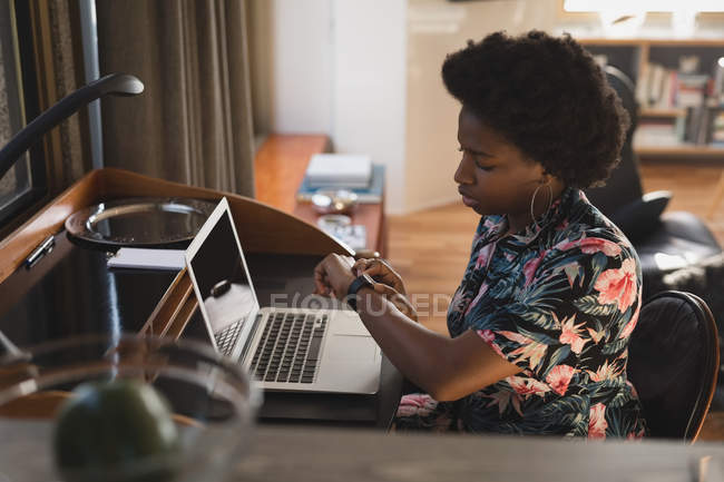Жінка використовує смарт-годинник під час роботи з ноутбуком вдома . — стокове фото