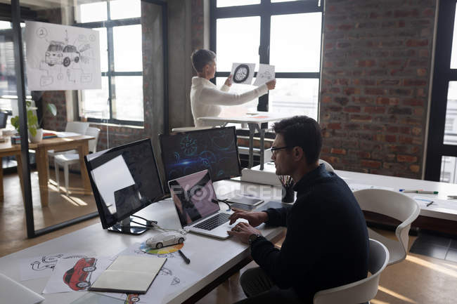 Businessman using laptop while colleague looking at sketch in office. — Stock Photo