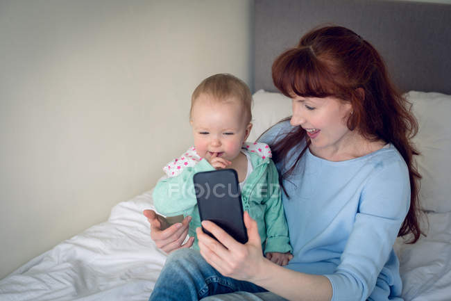 Madre e bambina scattare selfie con il telefono cellulare in camera da letto a casa — Foto stock
