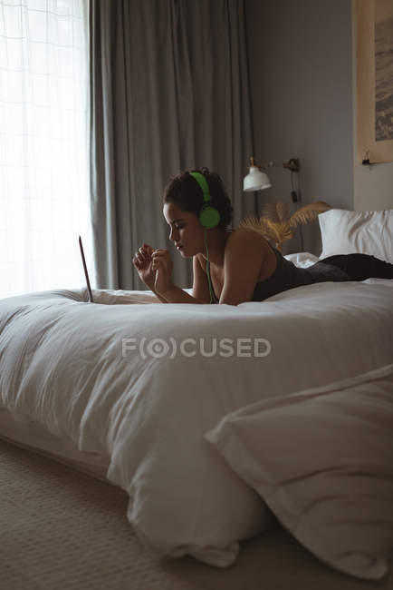 Femme utilisant un ordinateur portable tout en écoutant de la musique sur le lit dans la chambre — Photo de stock
