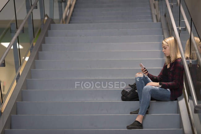 Teenage girl using mobile phone on staircase in university — Stock Photo
