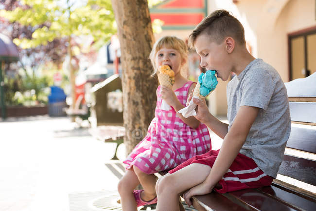 Geschwister essen an sonnigem Tag Eis auf Bank — Stockfoto