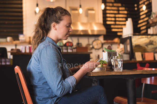 Donna che usa il cellulare mentre fa colazione a tavola nel caffè — Foto stock