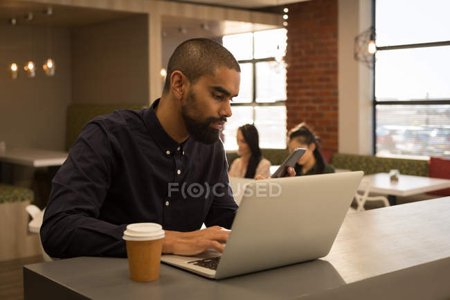 Executivo masculino trabalhando no laptop no refeitório no escritório — Fotografia de Stock