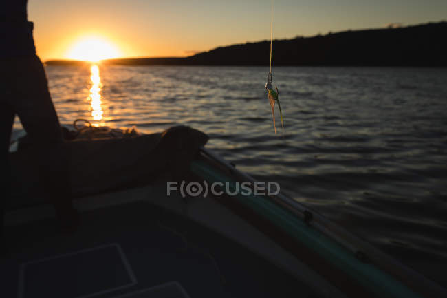 Vue en coupe de l'homme pêchant debout sur un bateau à moteur dans la rivière au coucher du soleil . — Photo de stock