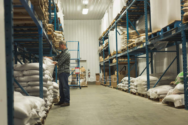 Mann richtet Getreidesack auf Regal in Fabrik ein — Stockfoto