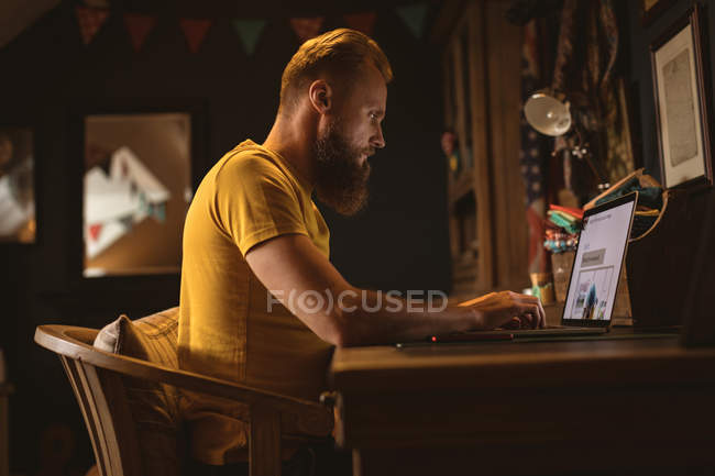 Человек сидит на стуле, используя свой ноутбук дома — стоковое фото