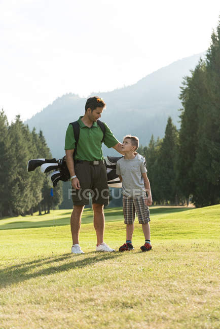Père et fils avec sac de golf interagissant les uns avec les autres dans le cours — Photo de stock