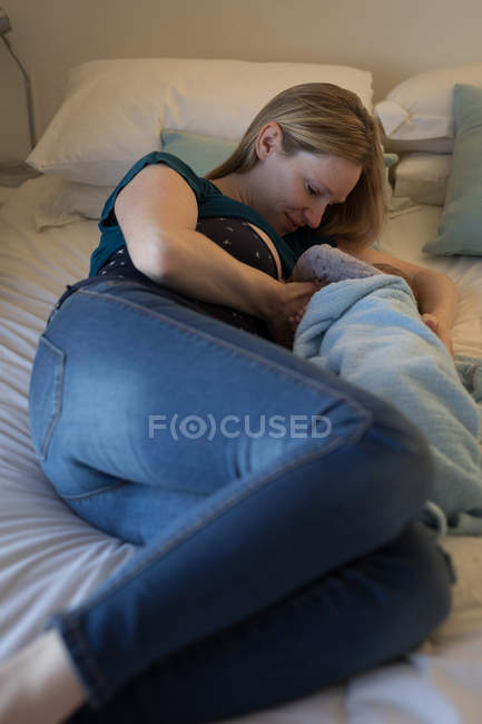 Mamma che tiene e allatta il bambino sul letto a casa . — Foto stock