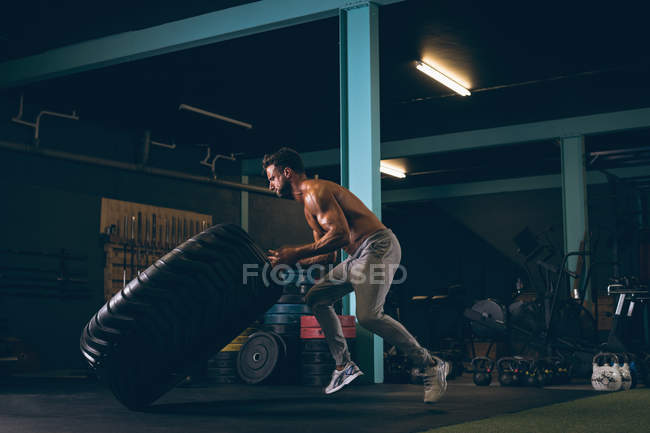 Homem musculoso exercitando com pneu pesado no estúdio de fitness — Fotografia de Stock