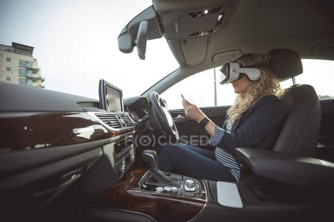 Side view of female executive using digital tablet and virtual reality headset in a car — Stock Photo