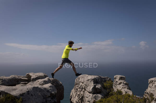 Hiker jumps from one cliff to another on a sunny day — Stock Photo