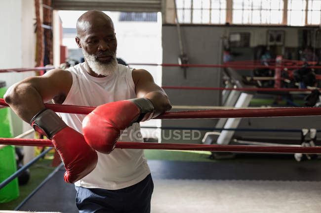 Старший мужчина в боксёрских перчатках стоит на ринге в фитнес-студии . — стоковое фото