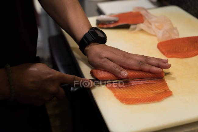 Chef filetea pescado en la cocina del restaurante en una tabla de cortar - foto de stock