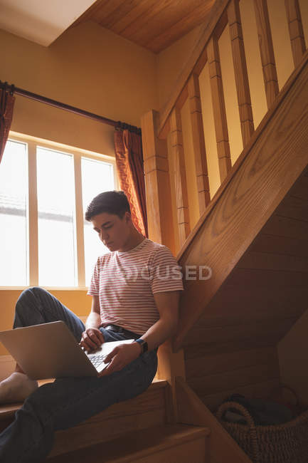 Homem usando laptop em escada de madeira em casa . — Fotografia de Stock