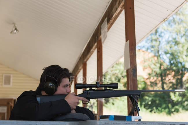 Un homme vise un fusil de sniper sur une cible dans un champ de tir par une journée ensoleillée — Photo de stock