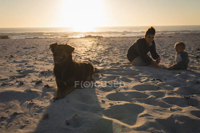 Mère et fils se relaxant sur le sable à la plage pendant le coucher du soleil — Photo de stock