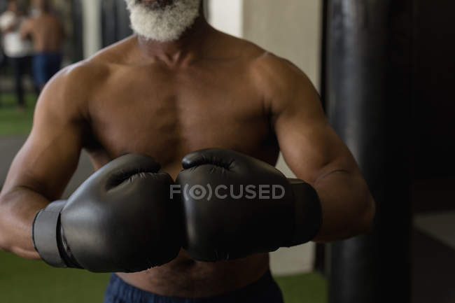 Mid section of senior man in black boxing gloves. — Stock Photo