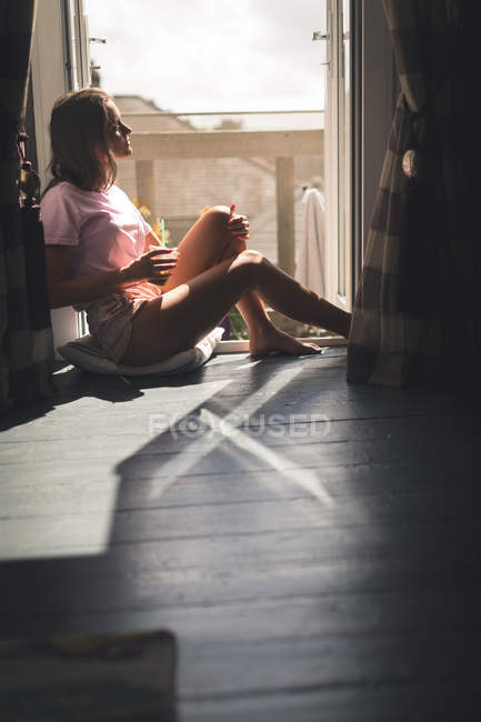 Frau sitzt am Fenster mit Kaffee und schaut zu Hause auf. — Stockfoto