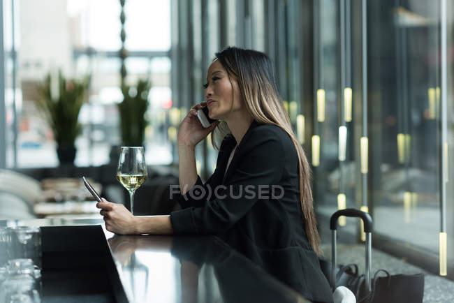 Asian businesswoman talking on the phone while using a digital tablet in lobby — Stock Photo