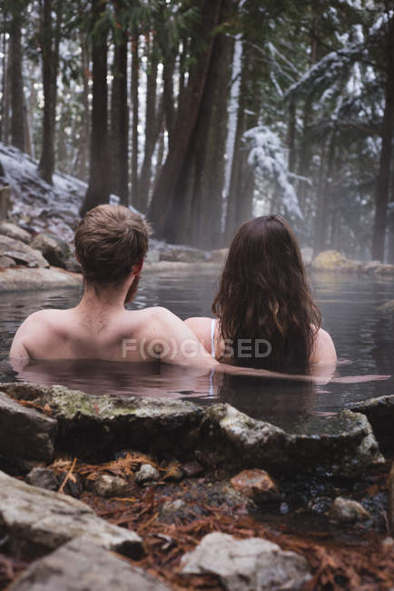 Vue arrière du couple se relaxant dans une source chaude pendant l'hiver — Photo de stock