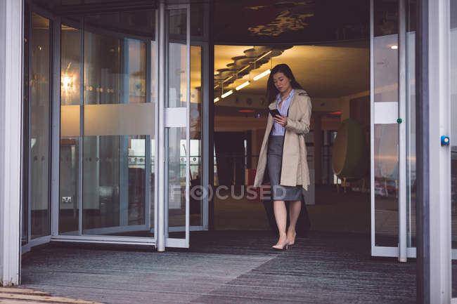 Geschäftsfrau benutzt Handy beim Verlassen des Hotels mit Gepäck — Stockfoto
