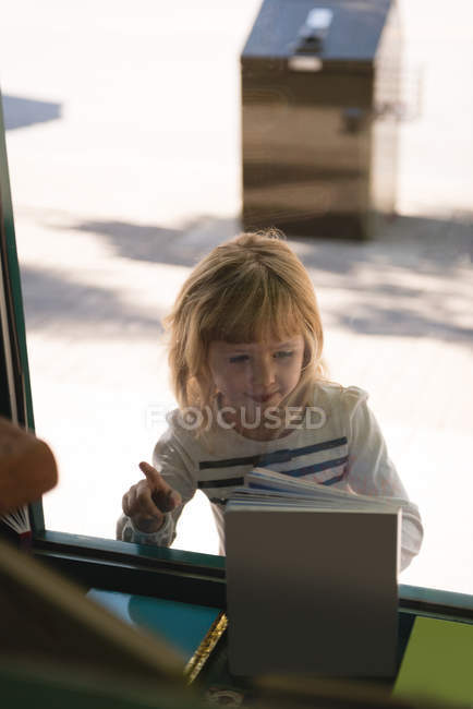 Chica espiando a través de la ventana de cristal fuera de la librería - foto de stock