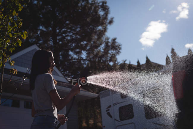 Sorrindo mulher lavando seu carro com um jato de água de alta pressão — Fotografia de Stock