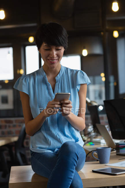 Улыбающаяся исполнительная женщина с помощью мобильного телефона на столе в офисе . — стоковое фото