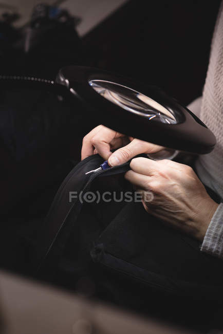 Alfaiate olhando através de lupa enquanto costura uma roupa na loja de alfaiate — Fotografia de Stock
