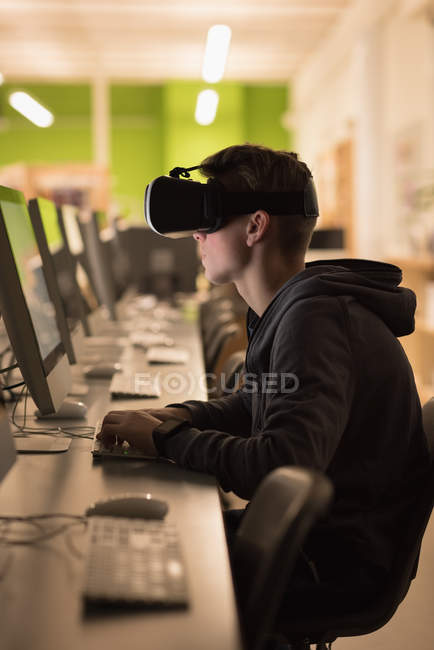 Adolescente usando fone de ouvido realidade virtual enquanto estudava em aula de informática na universidade — Fotografia de Stock