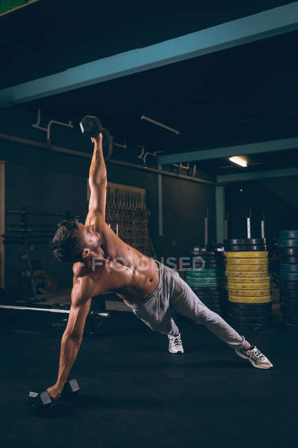 Homme musclé faisant push-up avec haltères dans le studio de fitness — Photo de stock