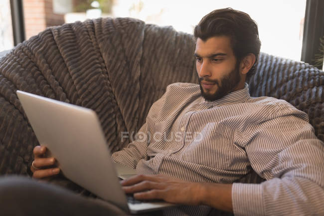 Homem usando laptop enquanto relaxa na cadeira de braço no café — Fotografia de Stock