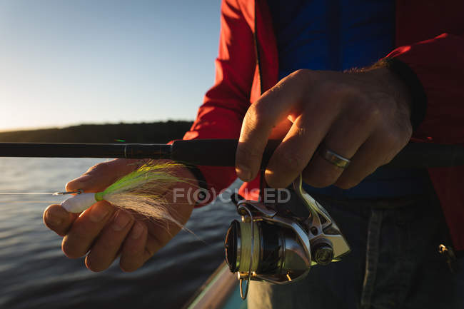 Крупним планом чоловічі руки зав'язують приманку в рибальському стрижні на моторному човні . — стокове фото