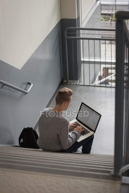 Vista posteriore del ragazzo adolescente che utilizza il computer portatile sulle scale — Foto stock