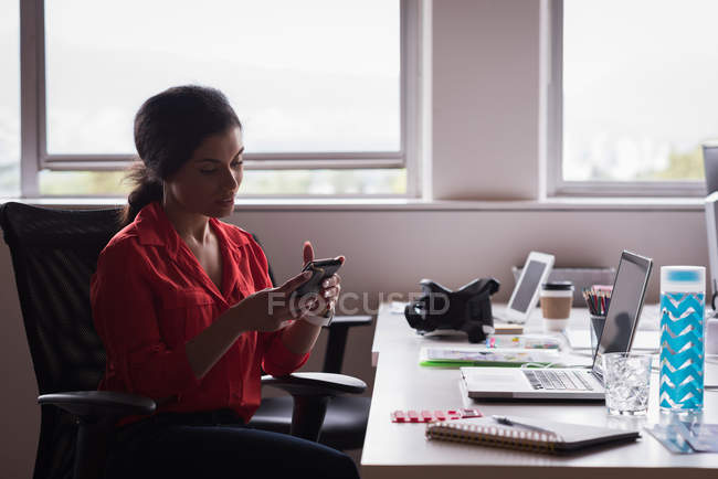 Жіночий керівник використовує мобільний телефон за столом у творчому офісі — стокове фото