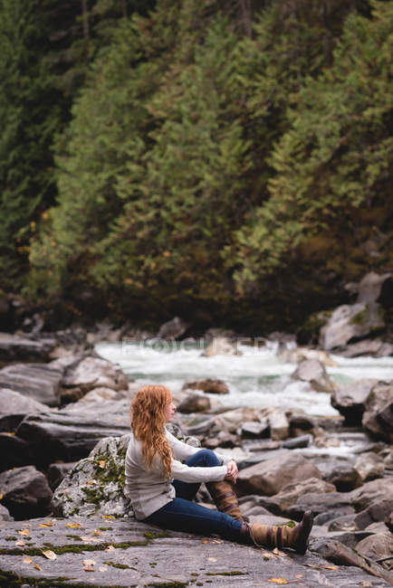 Femme assise sur la côte de la rivière dans la forêt — Photo de stock