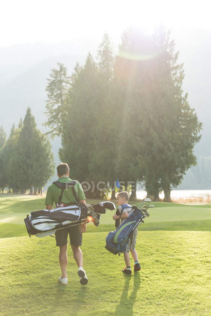 Pai e filho caminhando com saco de golfe em um dia ensolarado — Fotografia de Stock