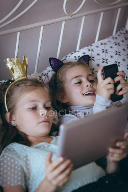 Geschwister mit Handy und digitalem Tablet auf Bett im Schlafzimmer — Stockfoto