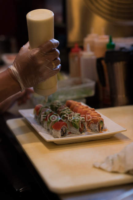Chef añadiendo salsa de mostaza sobre sushi en el mostrador de la cocina - foto de stock