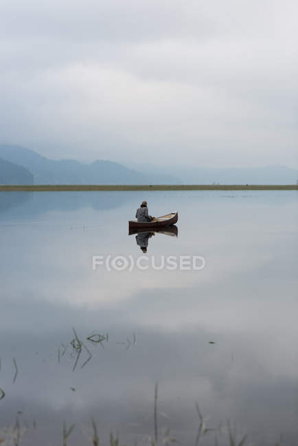 Mann auf Boot im stillen Fluss mit seinem Spiegelbild im Wasser — Stockfoto