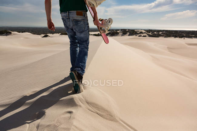 Человек идет с песчаной доской в пустыне в солнечный день — стоковое фото