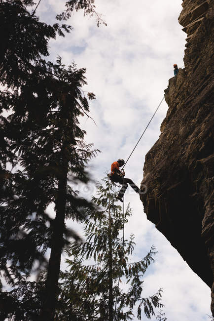 Vista a basso angolo dell'arrampicatore che sale sulla scogliera rocciosa — Foto stock