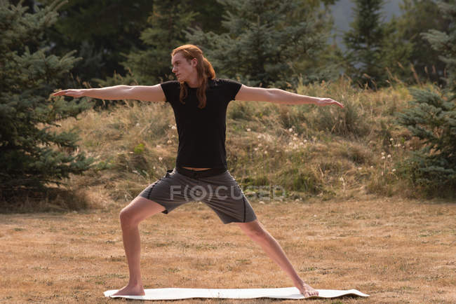 Hombre en forma realizando ejercicio de estiramiento en un terreno abierto un día soleado - foto de stock