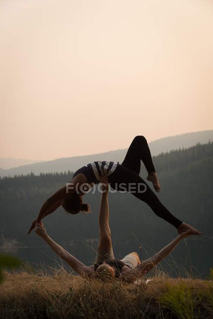 Спортивная пара, практикующая акро-йогу на пышной зеленой земле во времена Двана — стоковое фото
